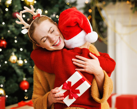 Happy family: loving mother hugging delighted son with Christmas present and closed eyesの写真素材
