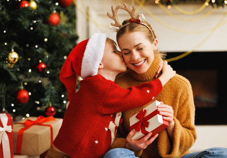 Cheerful family: child smiling embracing and kissing mother opening christmas presents together while celebrating holiday at homeの写真素材