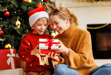 Cheerful family: smiling mother and cute son opening christmas presents together while celebrating holiday at homeの写真素材