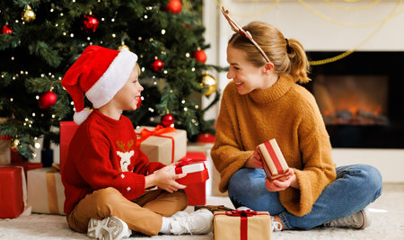 Cheerful family: smiling mother and cute son opening christmas presents together while celebrating holiday at homeの写真素材