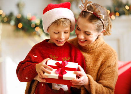 Cheerful family: smiling mother and cute son opening christmas presents together while celebrating holiday at homeの写真素材