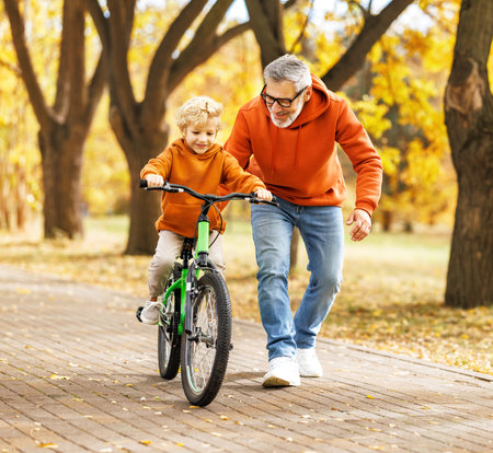Happy family grandfather teaches boy grandson to ride a bike in autumn park in natureの写真素材