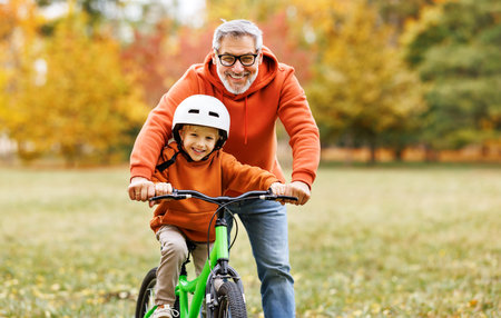 Happy family grandfather teaches boy grandson to ride a bike in autumn park in natureの写真素材