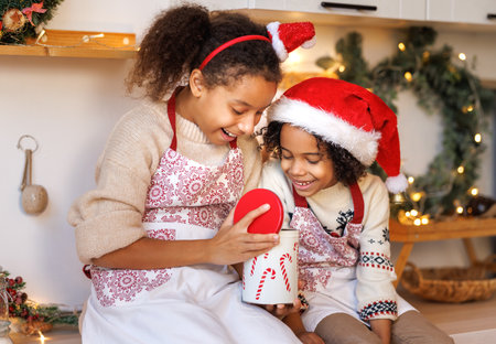 Happy funny african american kids on Christmas eve, girl and boy laugh and eat cookies that they baked together in cozy kitchen at homeの写真素材