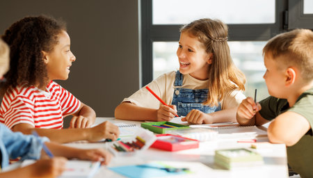 Positive multiracial students kids smiling and writing down data into notebook while sitting at table near classmates during test at schoolの写真素材