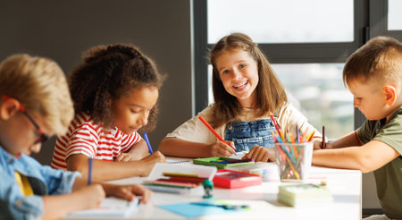 Positive multiracial students kids smiling and writing down data into notebook while sitting at table near classmates during test at schoolの写真素材