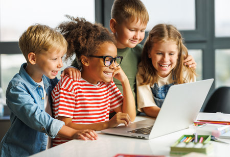 Positive kids pupils schoolchildren happy smiling, sitting at desk and looking at laptop screen during online lessonの写真素材
