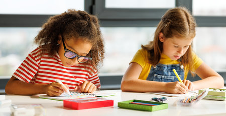 Focused multiracial students kids pupils school girls writing down data into notebook while sitting at table during test at schoolの写真素材