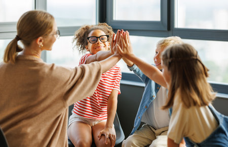 School psychologist with a group of school children conducts a mental health lesson, group therapy, a psychotherapy session and successful completion of collective school work in a bright officeの写真素材