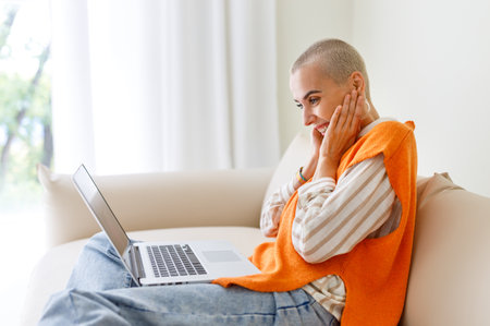 Beautiful woman freelancer with short hair works, makes video call and surprised gestures while sitting on sofa and working on laptop during work from homeの写真素材