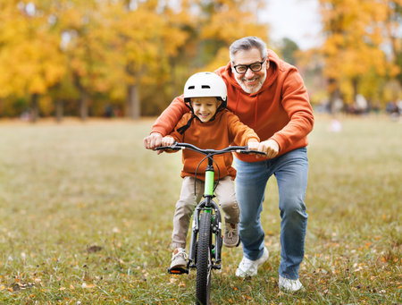 Happy family grandfather teaches boy grandson to ride a bike in autumn park in natureの写真素材