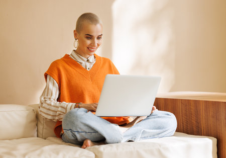 Full height of beautiful woman freelancer with short hair works, while sitting on sofa and resting on laptop during work from home in daytimeの写真素材