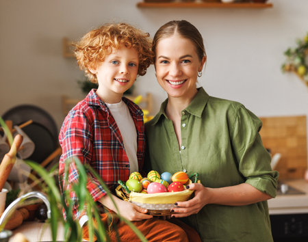 Easter Family Traditions. Loving mother and happy little kid son holding wicker basket full of painted multi-colored Easter eggs smiling in cozy light kitchen at homeの写真素材