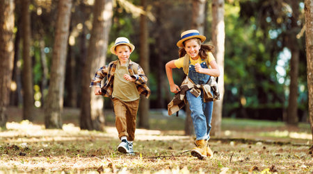Happy excited school children with backpacks in casual clothes enjoying walk in forest on sunny autumn day, two active kids boy and girl running and playing together during camping trip in natureの写真素材