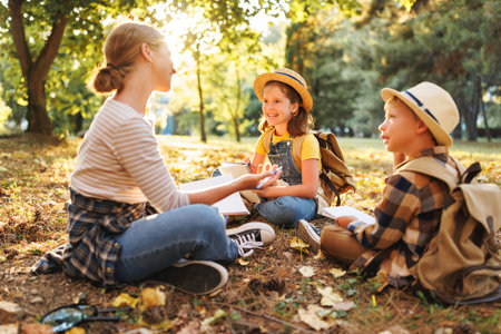 School activities in nature. Group of curious children and young female teacher sitting together on green grass in forest and learning about environment, boys and girls during ecology lesson in woodの写真素材