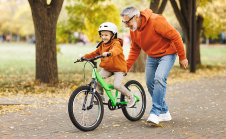 Happy family grandfather teaches boy grandson to ride a bike in autumn park in natureの写真素材