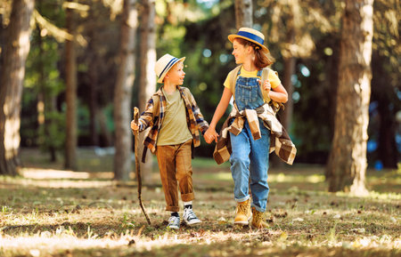 Happy excited school children with backpacks in casual clothes enjoying walk in forest on sunny autumn day, two active kids boy and girl running and playing together during camping trip in natureの写真素材