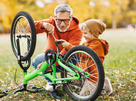 grandfather and grandson repair a bicycle together outdoors in the autumn parkの写真素材