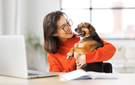 happy young female freelancer working on laptop remotely from home together with pet dogの写真素材