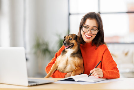 happy young female freelancer working on laptop remotely from home together with pet dogの写真素材