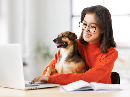happy young female freelancer working on laptop remotely from home together with pet dogの写真素材