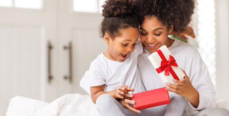 happy mother's day. african american baby daughter giving gift box to her mom for holiday in bed at homeの写真素材