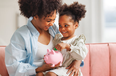 financial education. african american family, mother and child daughter with pig piggy bank counting savings at home on sofaの写真素材