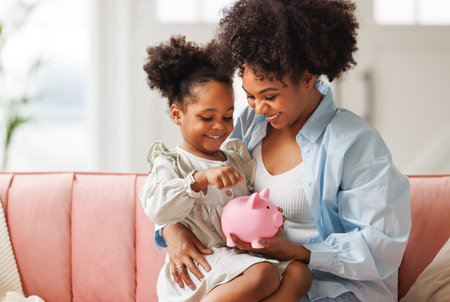 financial education. african american family, mother and child daughter with pig piggy bank counting savings at home on sofaの写真素材