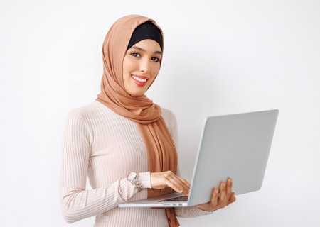 beautiful young muslim woman smiling and holding laptop in her hands on gray backgroundの写真素材