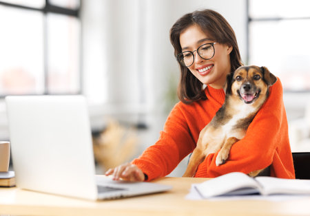 happy young female freelancer working on laptop remotely from home together with pet dogの写真素材