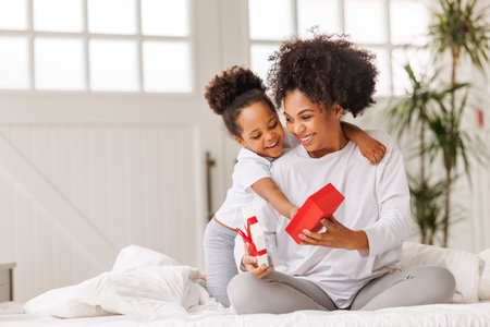 happy mother's day. african american baby daughter giving gift box to her mom for holiday in bed at homeの写真素材