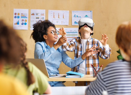 Innovation in education. Student schoolboy in virtual reality glasses together with teacher during lesson in bright classroom at schoolの写真素材