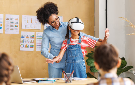 Innovation in education. Student schoolgirl in virtual reality glasses together with teacher during lesson in bright classroom at schoolの写真素材