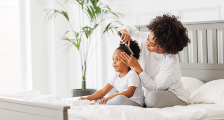 happy ethnic family. African american mother brushing her little daughter's curly hairの写真素材