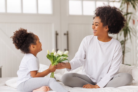 Happy mother's day! Afro american family happy baby daughter congratulations mom on the holiday gives bouquet of flowers at homeの写真素材