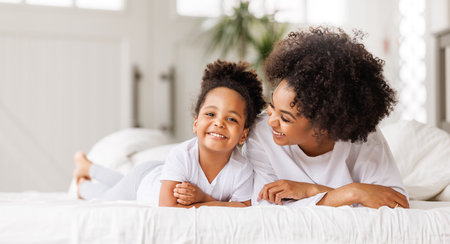 happy ethnic family. African american mother and daughter play and laugh in bed an homeの写真素材