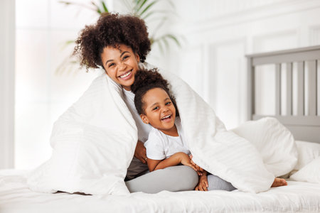 happy ethnic family. African american mother and daughter play and laugh in bed an homeの写真素材