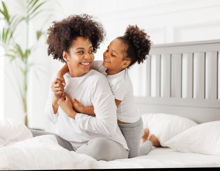 happy ethnic family. African american mother and daughter play and laugh in bed an homeの写真素材