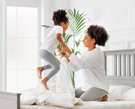 happy ethnic family. African american kid jumping, play and laugh on bed with mother an homeの写真素材