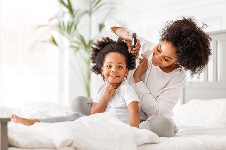 happy ethnic family. African american mother brushing her little daughter's curly hairの写真素材