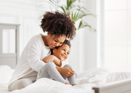 happy ethnic family. African american mother and daughter play and laugh in bed an homeの写真素材