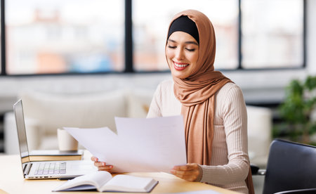 beautiful young smiling muslim woman in traditional religious hijab works remotely on laptop from homeの写真素材