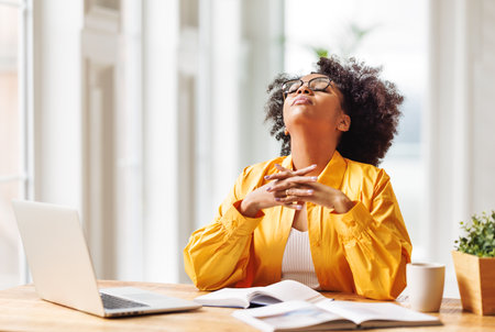 Frustrated tired young african american woman entrepreneur closed eyes with painful expression on her face, sitting in front of laptop working remotely online. Frustrated ethnic female has computer problemの写真素材
