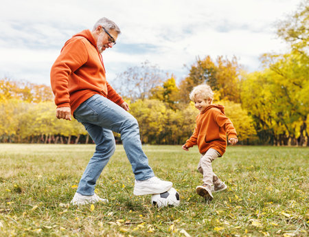 Happy family grandfather and grandson play football on lawn in the parkの写真素材