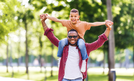 Happy african american family father and son have fun on walk in summer parkの写真素材