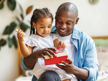 happy fathers day. African american baby daughter giving gift box to her dad for holiday at homeの写真素材