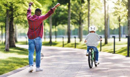 Happy family father teaches boy son to ride bike in park in natureの写真素材