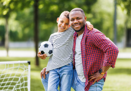 Portrait of happy father and son with ball while playing football on green grass in summer parkの写真素材
