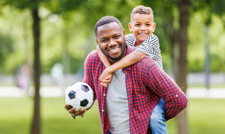 Portrait of happy father and son with ball while playing football on green grass in summer parkの写真素材