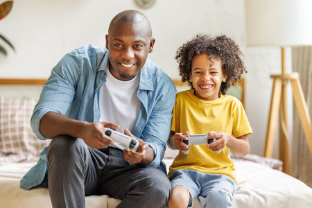 Happy african american family father and son playing video game console at homeの写真素材